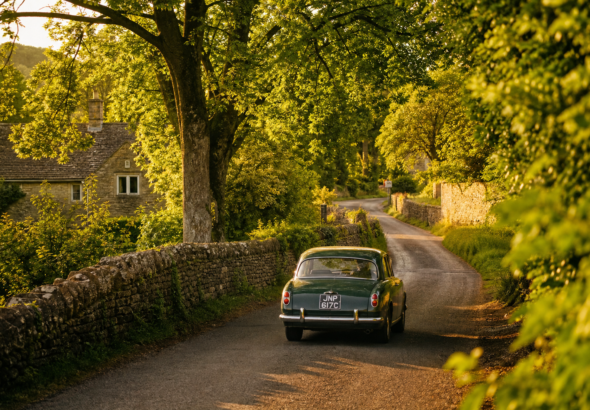 A vintage car driving down a scenic, tree-lined country lane.